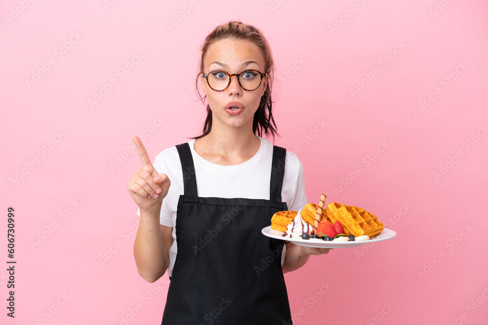 Restaurant waiter Russian girl holding waffles isolated on pink background intending to realizes the solution while lifting a finger up Restaurant waiter Russian girl holding waffles isolated on pink background intending to realizes the solution while lifting a finger up