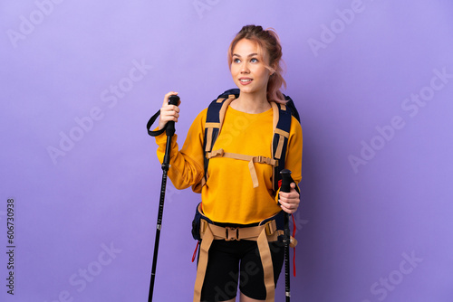 Teenager girl with backpack and trekking poles over isolated purple background thinking an idea while looking up