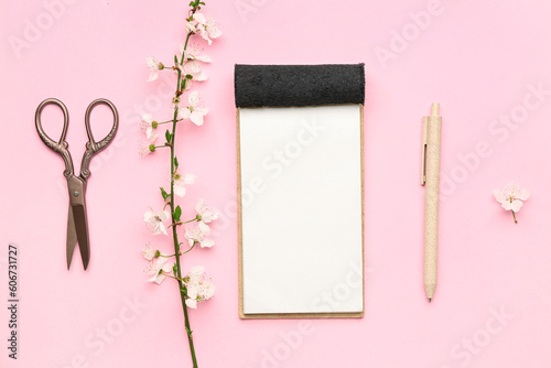 Composition with blooming tree branch, notebook, pencil and scissors on pink background