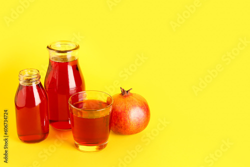 Bottles and glass of fresh pomegranate juice on yellow background