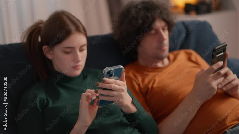 young couple lying on couch at home after work and both looking in their smartphones. people spending time together but with own phones, looking and posting social networks, messagers