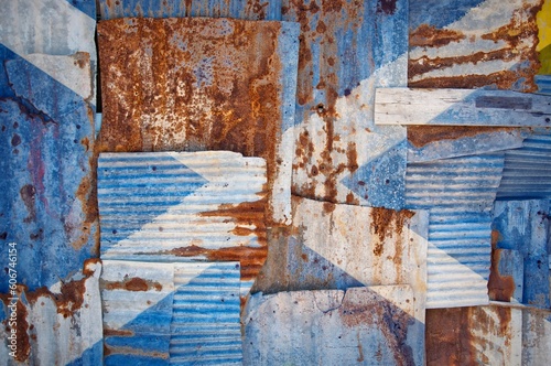 Flag of Scotland painted onto rusty corrugated iron sheets overlapping to form a wall or fence © Tonygers/Wirestock Creators