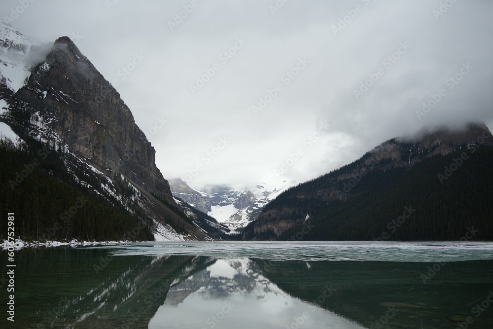 Forest and mountains reflected in Vermilion Lake in Banff National Park in winter under cloudy sky