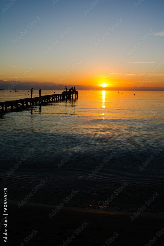 Silhouette of dock with people in sea during sunset