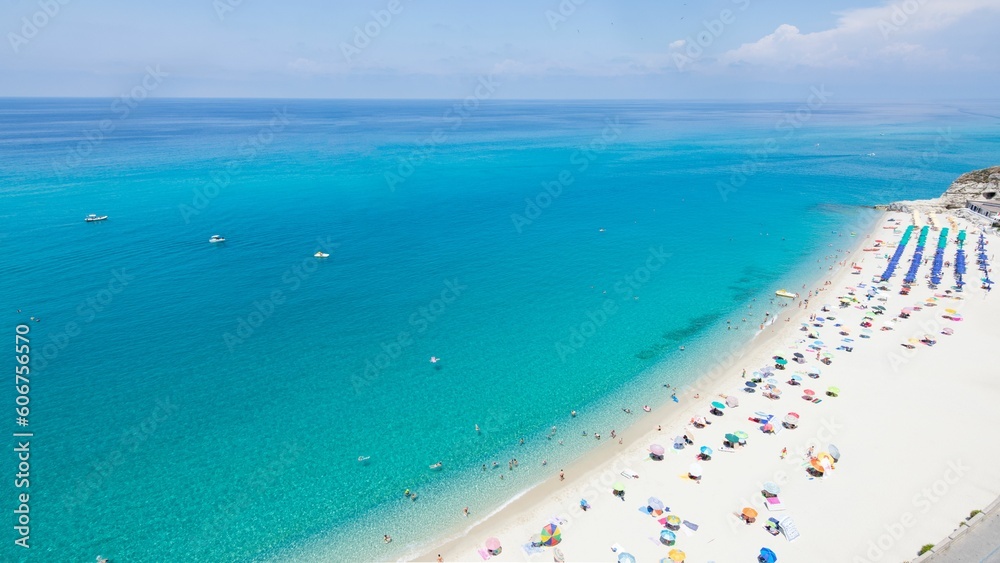 Aerial view of a sandy beach with colorful table umbrellas under blue sky in Sicily coast, Italy