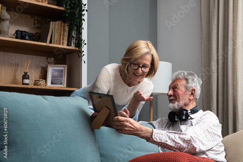 Happy senior couple having fun at their cozy warm home. Elderly man and elderly woman simple living enjoying their retirement with books, laptop, smiling and talking about memories.