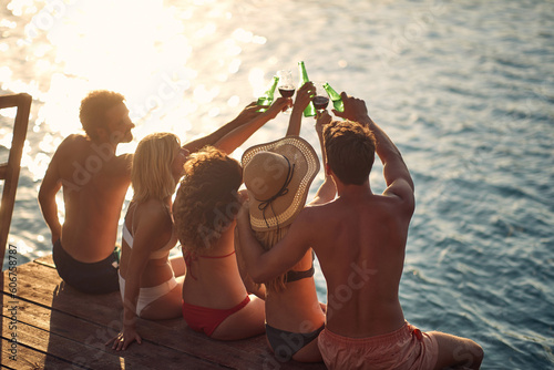 Happy group of  people toasting with beer on a dock by the river during the summer sunny day
