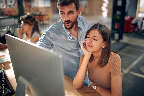 Office workers in front of computer desktops discussing project, man pointing on screen, woman colleague feeling annoyed, not liking his idea.