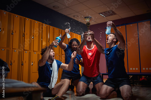 Group of four men team players in locker room celebrating success together, holding golden medal and screeming of joy, splashing water. photo