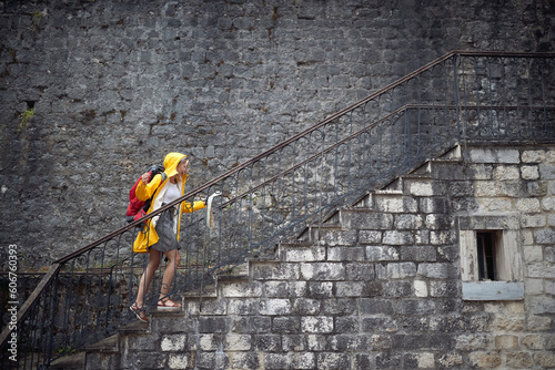 Young blonde tourist in raincoat going up stairs looking at map, feeling victorious. Ariving at her destination. Travel, city, lifestyle concept. photo