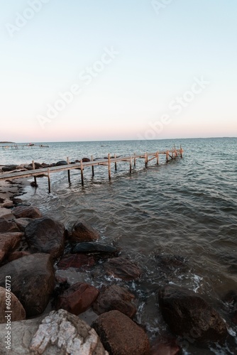 Vertical shot of a wooden pier on a rocky shore at sunset in Denmark