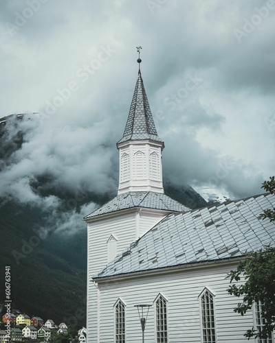 Vertical of the white Hyen church in Norway with a mountain hiding behind a cloud in the background photo