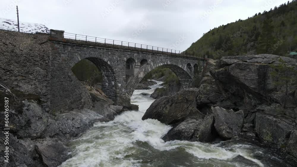 Drone view over the flowing river under the old stone bridge in the mountains