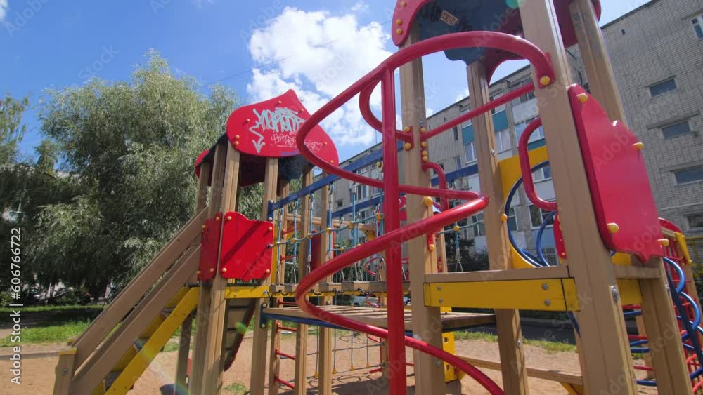 Entertaining equipment for children installed on playground. Residential building and lush green trees under blue sky on sunny summer day Entertaining equipment for children installed on playground. Residential building and lush green trees under blue sky on sunny summer day