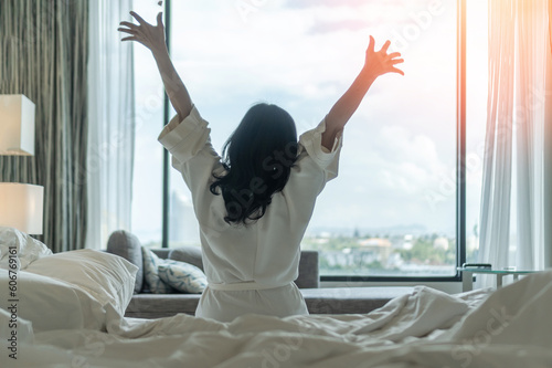 Hotel relaxation on lazy day with Asian woman waking up from good sleep on bed in weekend morning resting in comfort bedroom celebrating having happy work-life quality balance lifestyle