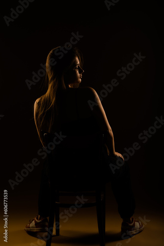 A back view photo of a girl posing while sitting on a chair in studio