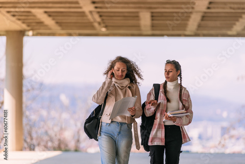 Brunette girl carrying books walking and explaining something to her curly haired friend