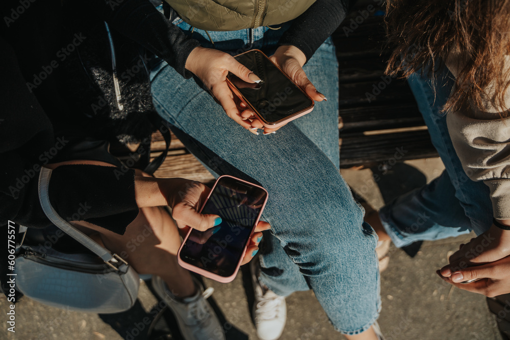 Close up shot of girl showing something on the phone to her friends. They are sitting on a bench in the park