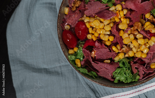 Deli meat cold cut  with vegetables, cherrry tomatoes, sweet corn, walnuts and lettuce salad leaves in salad served on kitchen textile cloth and dark background photo