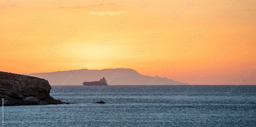 Sunset over Greek island as line ship leaves Cyclades. Sun colors the sky. Blue Aegean sea. Space