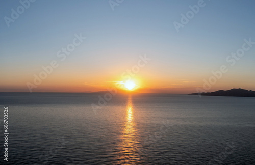 Sunset over Cyclades island Greece. Golden sun gets hide behind hill and colors gold sea water.