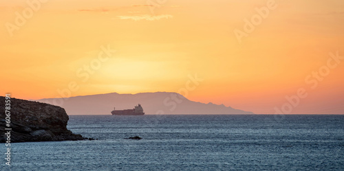 Sunset over Greek island as line ship leaves Cyclades. Sun colors the sky. Blue Aegean sea. Space