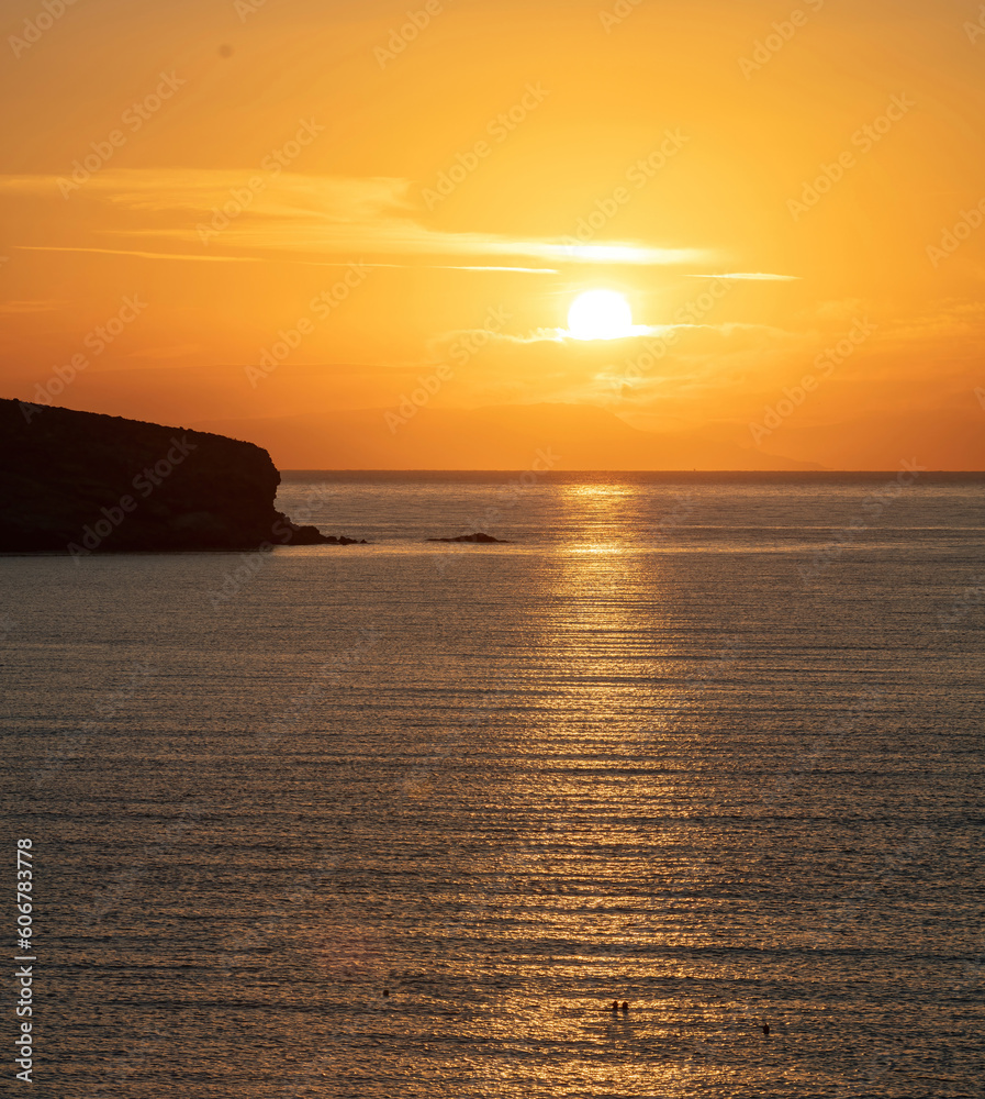 Summer sunset over Greek island, Cyclades, Greece. Golden sun colors the sky and makes sea sparkle.