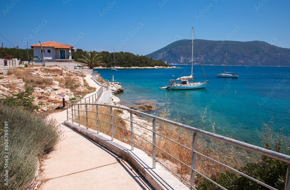 Left ruins of ancient Roman cemetery and right turquoise water with 2anchored sailboats off Fiscardo village sea coast. 