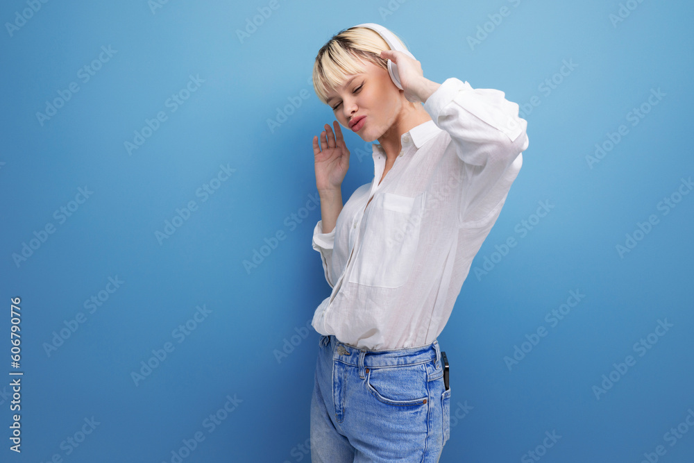 young positive caucasian woman with a short haircut dressed in a white shirt and jeans uses wireless white headphones on an isolated background with copy space. concept of devices for music young positive caucasian woman with a short haircut dressed in a white shirt and jeans uses wireless white headphones on an isolated background with copy space. concept of devices for music