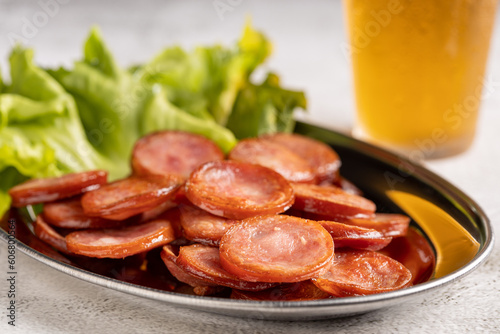 Sliced ​​fried pepperoni sausage with glass of beer on the table.
