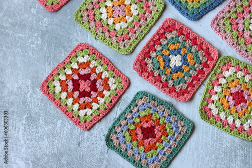 Colorful crochet Granny squares on light grey background with copy space. Handmade blanket in process. Multicolored vintage ornament. Hippie fashion concept. 
