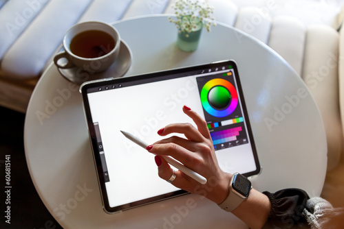 A girl in a cafe draws with a stylus on a graphics tablet.