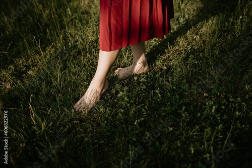 a barefoot girl in a red dress is standing on the grass