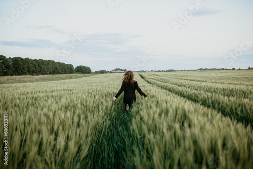 girl in a black jacket runs across a field of wheat