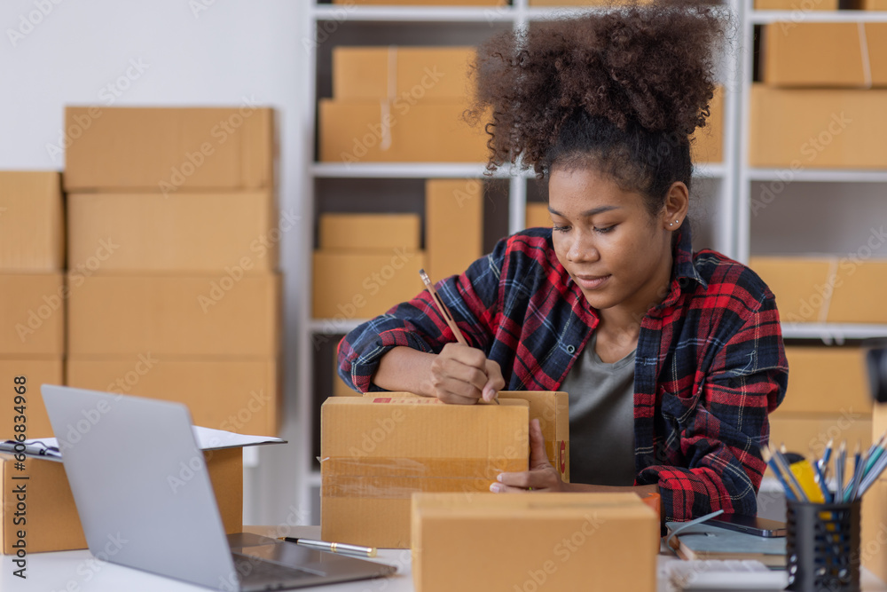 Portrait of Young African American business woman SME e-commerce employee sitting at home full of packages write note of orders use a calculator and laptop online SME business idea concept
Portrait of Young African American business woman SME e-commerce employee sitting at home full of packages write note of orders use a calculator and laptop online SME business idea concept