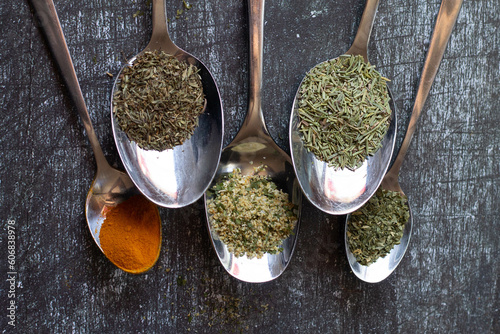 Quadro su tela Spoons with spices and herbs on a black background