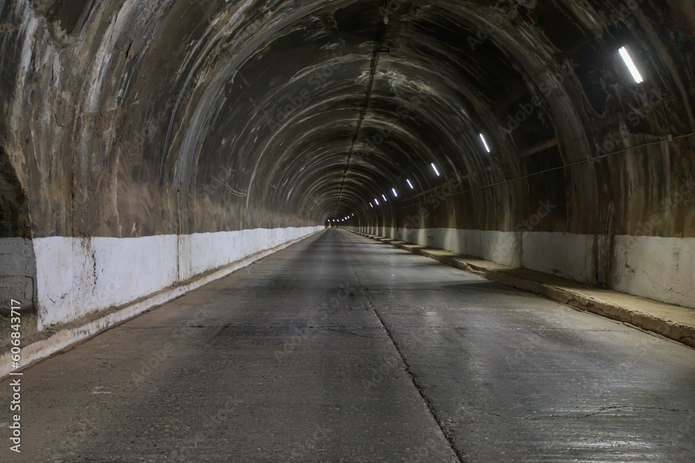 Tunnel with road inside mountain with arch dam.