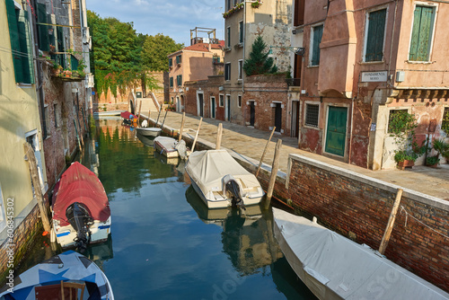 Boats covered from rain parked in the water next to the house in canal of Venice. Water transport and transportation theme.