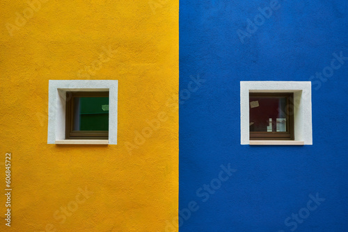 colorful house facade on Burano island, north Italy. Half orange half blue house wall with a yellow door and two windows with plants in it © Ryzhkov Oleksandr