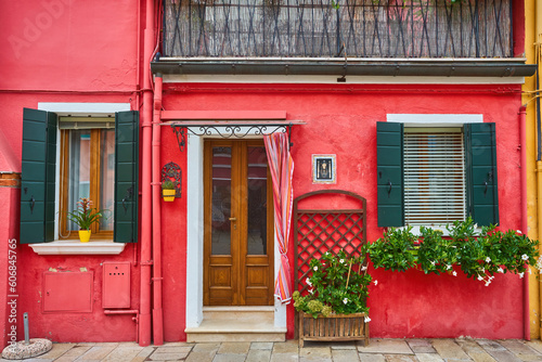 Door and window with flower on the red facade of the house. Colorful architecture in Burano island, Venice.