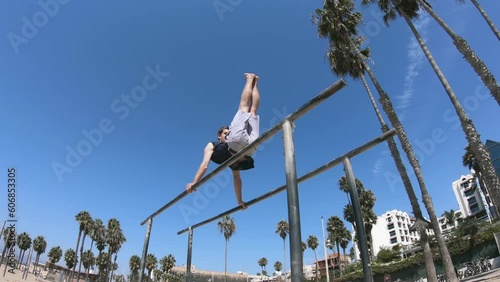 Handsome fit young man exercising on the bars under the palm trees in the famous californian beach in Venice beach photo