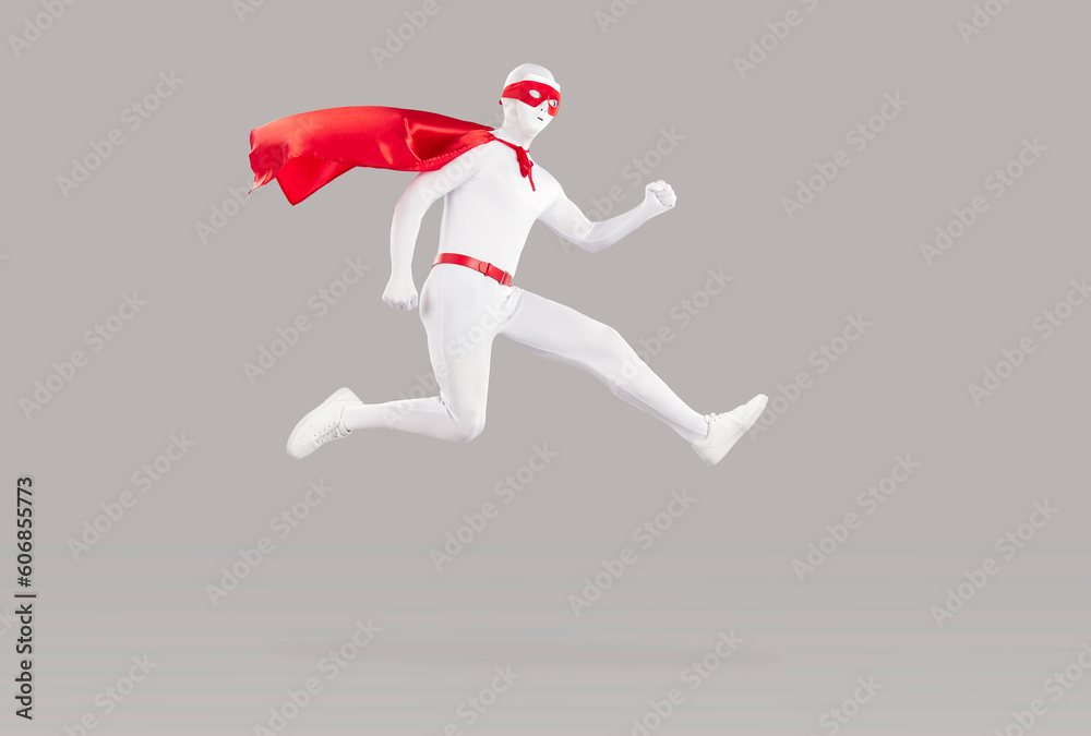 Φωτογραφία Funny super hero in a red cape, eye mask and white bodysuit flying in the air on a gray color background