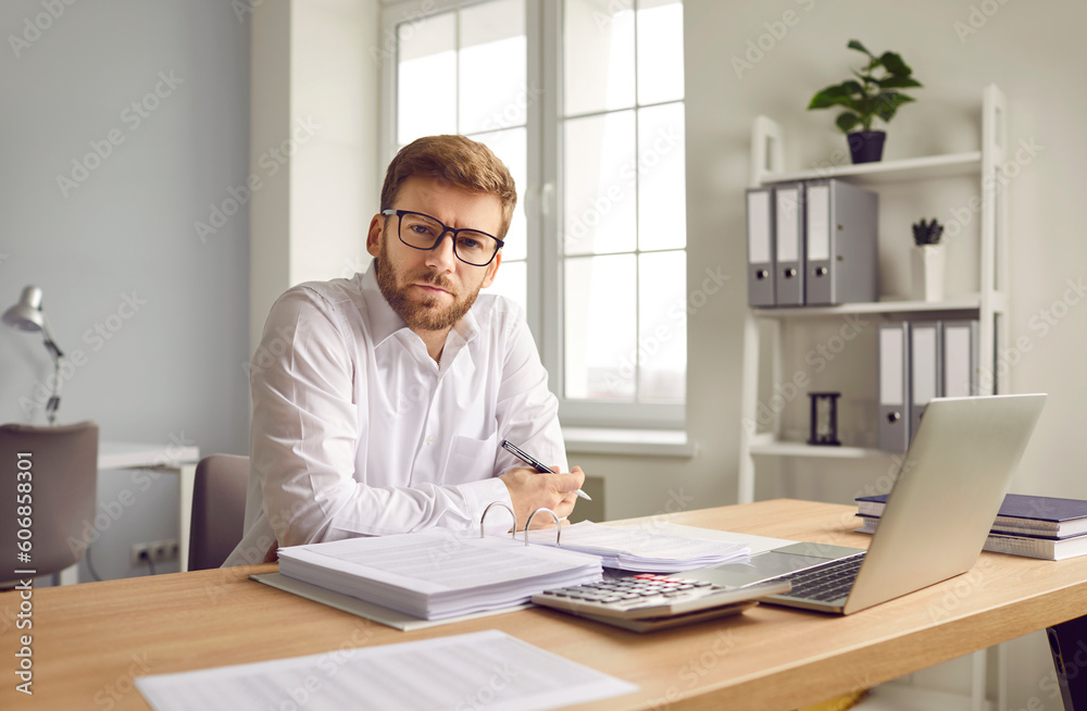 Businessman sitting at computer and filling report in office. Portrait of man accountant wearing glasses working and analysing financial documents at workplace. Financial manager, bookkeeper Businessman sitting at computer and filling report in office. Portrait of man accountant wearing glasses working and analysing financial documents at workplace. Financial manager, bookkeeper