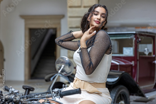 Young woman with long black hair is sitting seductively on a vintage motorcycle. Horizontally. 