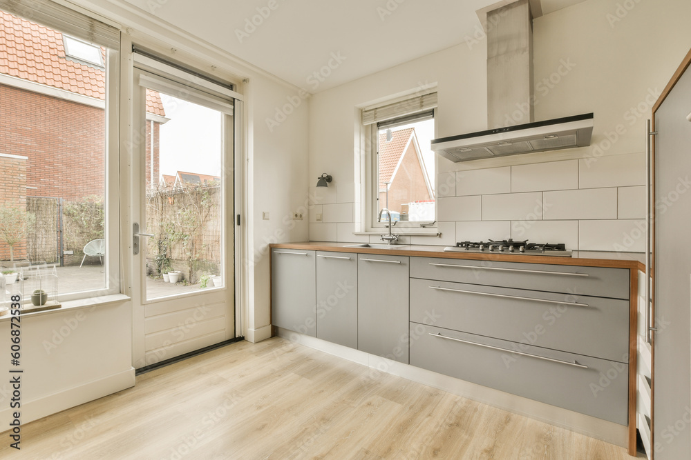 Fototapeta premium a kitchen with wood flooring and white tile on the walls, in front of an open window looking out onto a brick wall