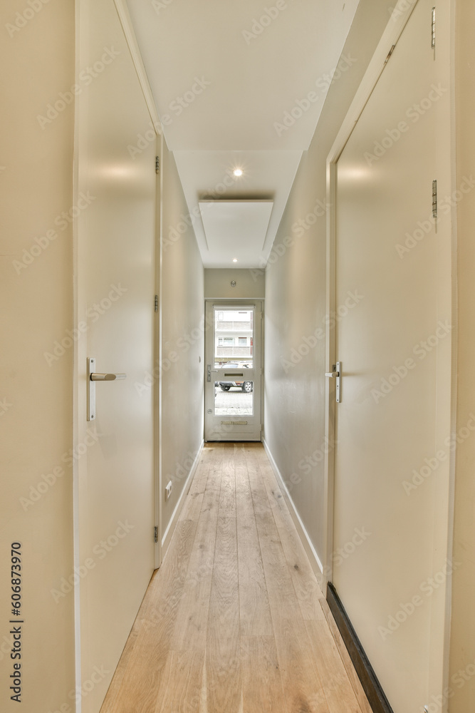 a long hallway with white walls and wood flooring on both sides, leading to an open door that leads to the living room
