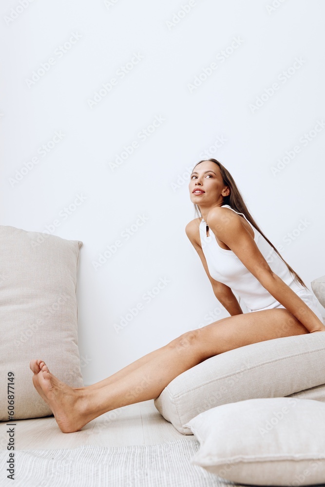 A beautiful woman with tanned skin and a beautiful snow-white smile with teeth and brown natural long hair on her head poses on a white background of a house with pillows A beautiful woman with tanned skin and a beautiful snow-white smile with teeth and brown natural long hair on her head poses on a white background of a house with pillows