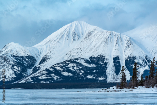 Incredible snow capped mountains in the winter time with a frozen lake in foreground. Taken in Atlin, British Columbia near Alaska, Yukon Territory, Canada.  photo