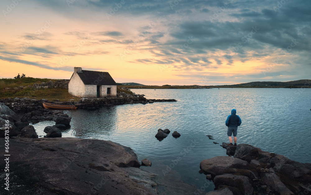 Beautiful sunset nature scenery with man on the rock watching sunrise at Fisherman's hut, screebe, connemara national Park in County Galway, Ireland