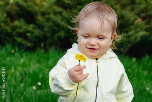 one year old happy blond baby boy playing outside in the garden with a yellow flower